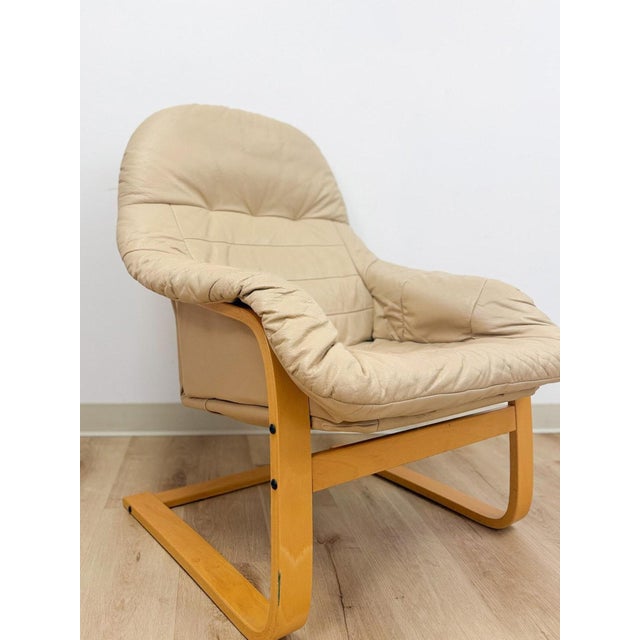 This elegant vintage Danish made tan leather cantilever armchair is a refined and collectible mid-century modern seating...