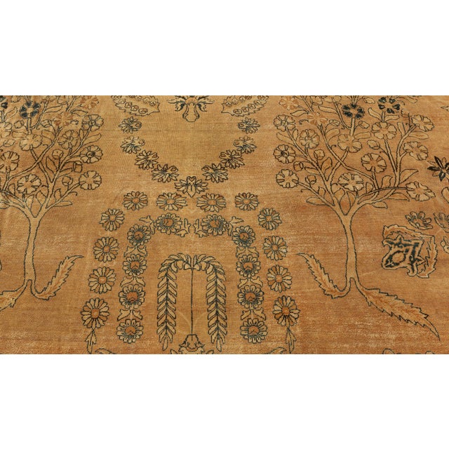 A decorative early 20th century Persian Kirman (Kerman) antique rug, the spacious camel field with a mirrored overall...
