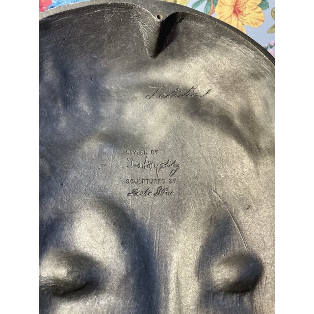 Striking metal face sculpture titled “Letitia,” representing the Roman goddess of joy and gladness, with a softly...