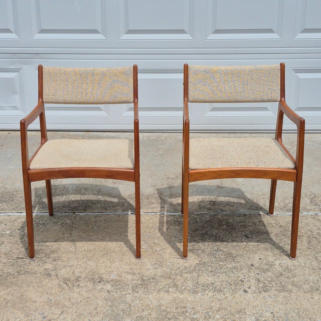 This is a pair of Danish modern style teak arm chairs by D-Scan. The chairs have solid teak frames with sleek midcentury...