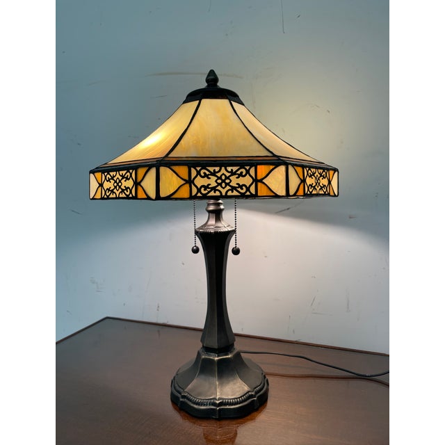 Vintage table lamp featuring a paneled shade with warm amber and cream tones. The shade is constructed from multiple glass...