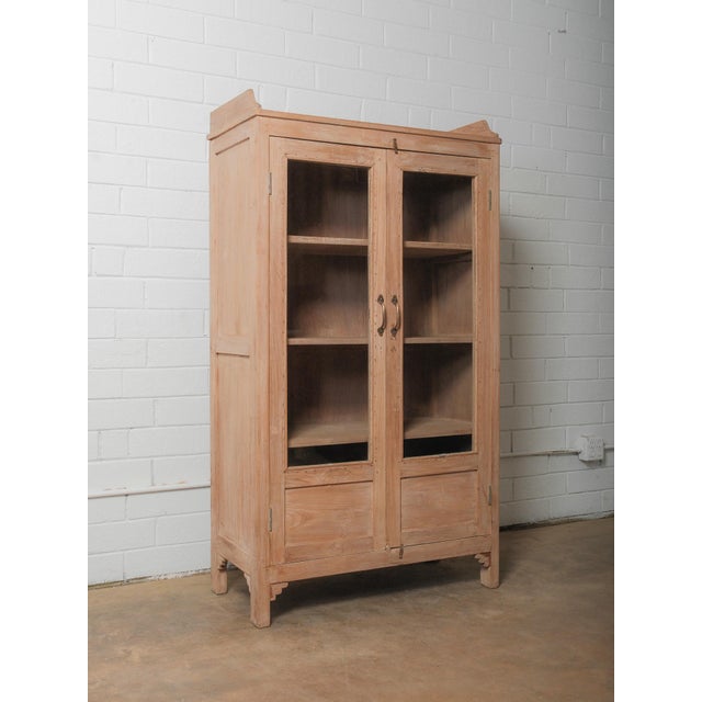 A quietly monumental display cabinet rendered in pale, raw-finished hardwood, its presence defined by architectural...
