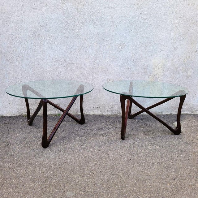 Rare pair of round coffee tables with glass tops, resting on sculpted varnished wood bases. The base of each table is...