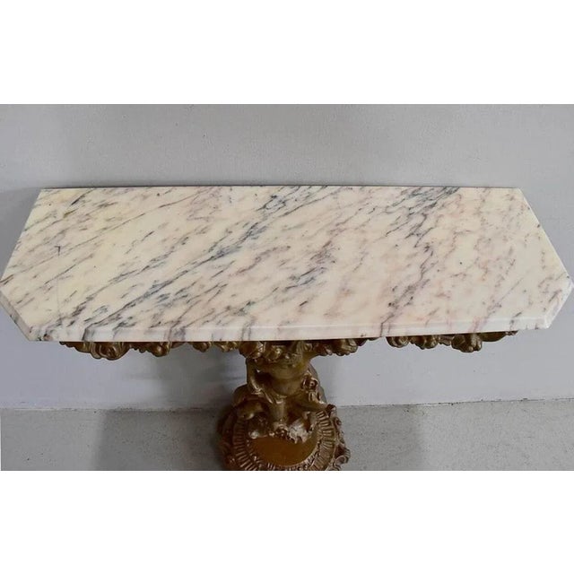 Small carved wooden console and patinated bronze with its old marble top cream streaked with gray and pink. The belt is...