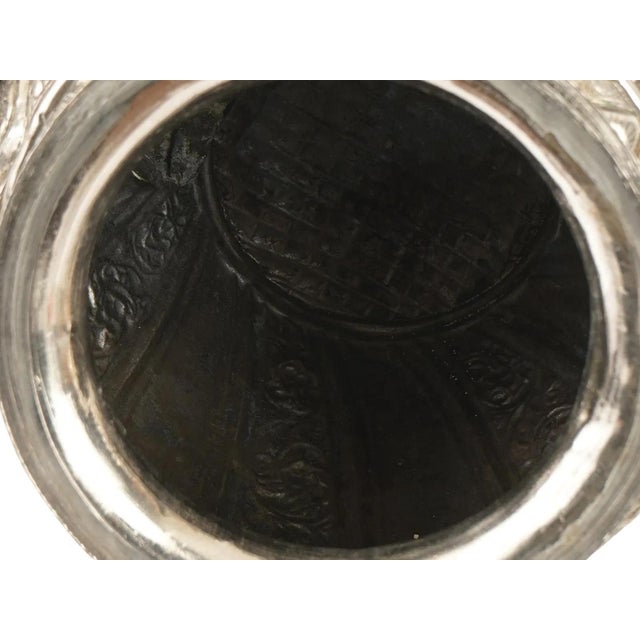 A Tibetan ewer crafted from a silver alloy featuring intricate repousse and chased ornamentation across its globular body,...
