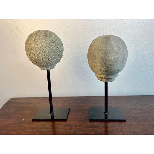 Pair of spheres mounted on iron bases. One is 19th century and is made of stone. The second sphere is made of cement and...