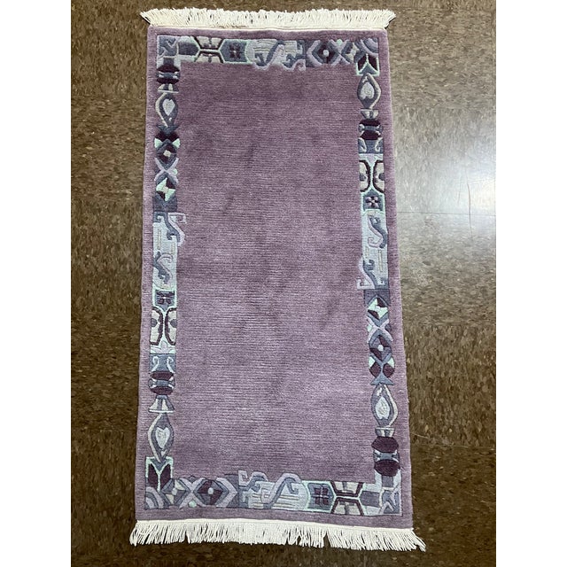 Hand-knotted Nepal wool rug featuring a solid mauve field framed by a decorative border with stylized geometric motifs....