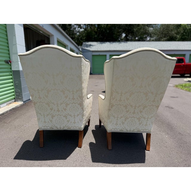 Timeless Ethan Allen Selby wing chairs upholstered in an elegant ivory tone-on-tone damask fabric with nailhead trim and...