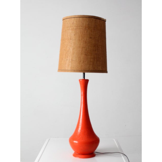 Vintage mid-century ceramic table lamp showcasing a striking sculptural silhouette and a vibrant orange glazed finish. The...