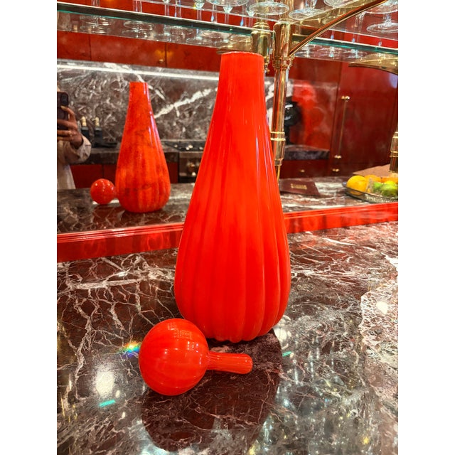 A striking Italian art glass “Circus Bottle” in a vivid orange hue. The sculptural design features an elongated, tapered...