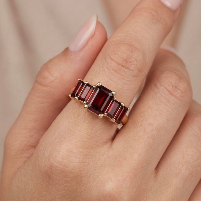 Embrace rich, passionate warmth with this striking three-stone ring, featuring a trio of deep garnet-red emerald-cut...