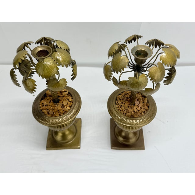 A charming pair of mid-20th-century brass candlesticks modeled as stylized palm trees rising from classical urn-form...