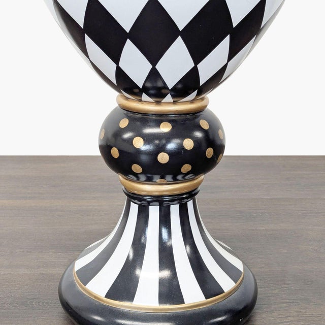 This MacKenzie-Childs vase features a bold black and white harlequin pattern with gold accents. The pedestal base adds...