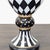This MacKenzie-Childs vase features a bold black and white harlequin pattern with gold accents. The pedestal base adds...