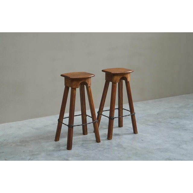 A pair of mid century bar stools in solid oak and wrought iron. Europe, 1960s. These bar stools feature a modest yet very...