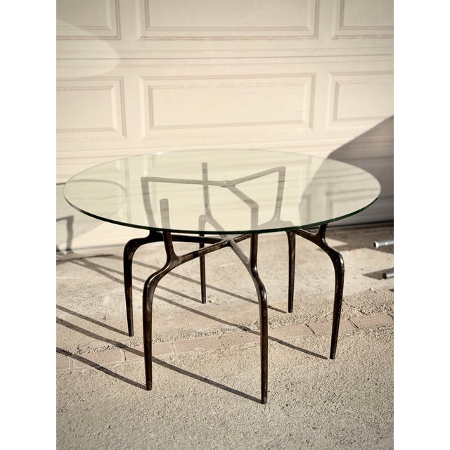 Sculptural Cyrano dining table by Made Goods featuring an organically formed bronzed iron base and thick round glass top....
