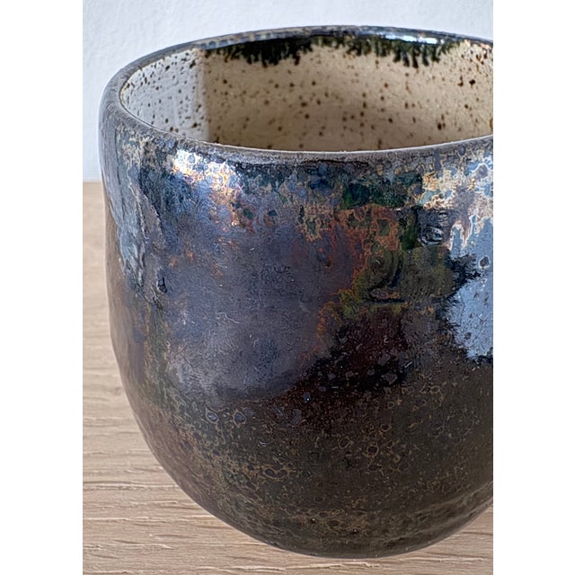 A small studio pottery cup with a softly rounded cylindrical form and a richly atmospheric glaze. The exterior is finished...