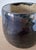 A small studio pottery cup with a softly rounded cylindrical form and a richly atmospheric glaze. The exterior is finished...