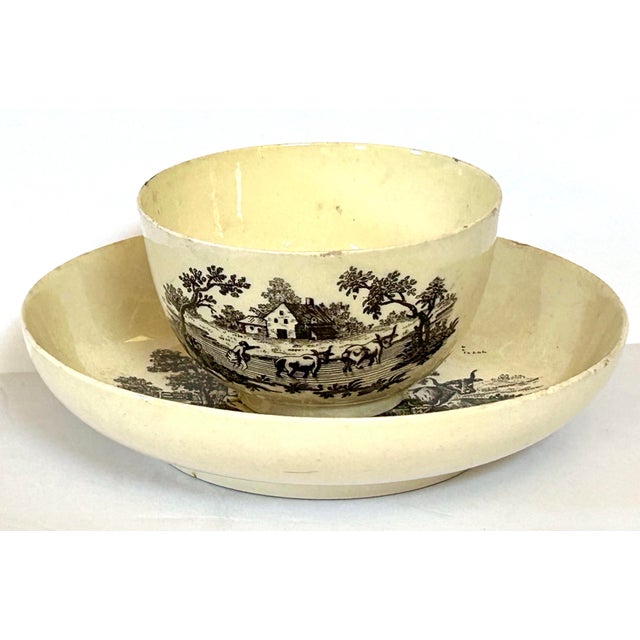 18th-century English George III creamware matching set of tea bowl and saucer featuring black transfer-printed country...