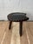A striking hand-carved rustic tripod stool featuring deeply sculpted organic detailing and a dark leather upholstered seat...