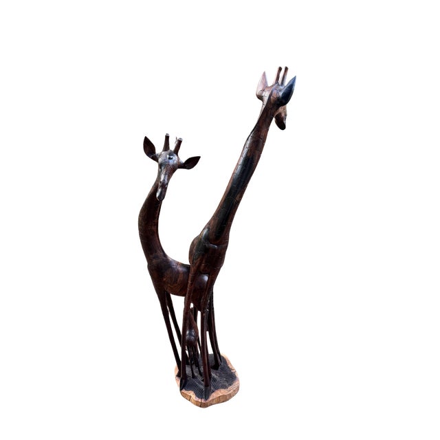 Hand-carved from a single solid hardwood log, this sculptural giraffe family depicts two adult giraffes with a nursing...