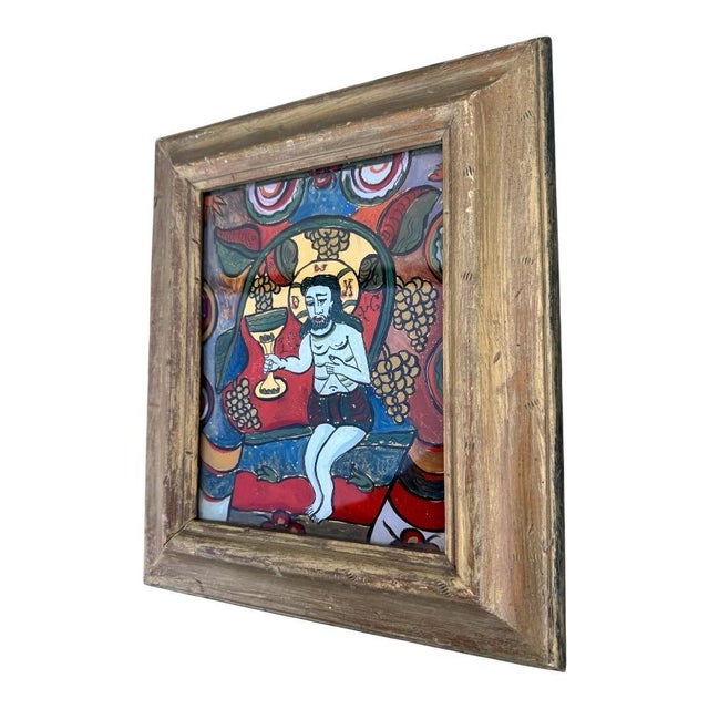 A vintage reverse-painted glass folk art depicting Christ holding a Eucharistic chalice, rendered in a vibrant palette of...