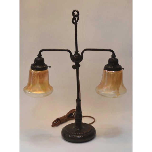 Tiffany Studios two light bronze favrile table lamp. Two bell-shaped favrile glass signed iridescent shades supported by...