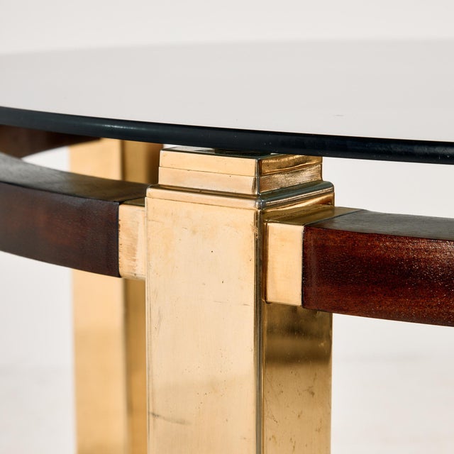 A dining table with classic lines from the 1970s. The table has a mahogany and brass frame, a smoked glass top, and the...