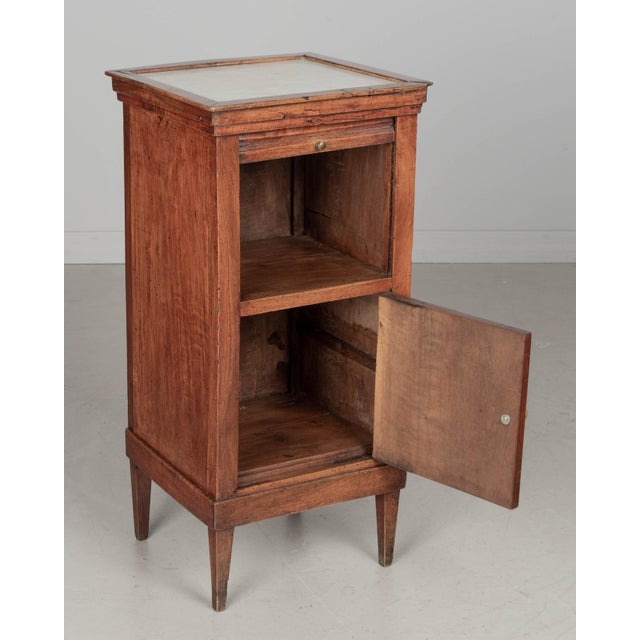 A 19th century French Country walnut side table, or nightstand, with a vertical tambour door above a cabinet door. Inset...