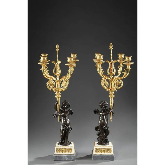 Exquisite pair of candelabra, composed of a young cupid on clouds in patinated bronze, holding an ormolu torch. A vase...