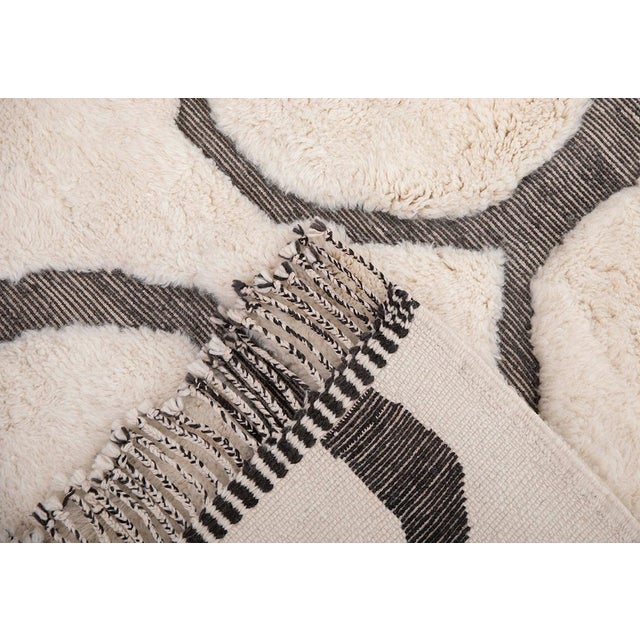 Artistic hand-knotted wool rug in Midnight Black and Ivory, adorned with a distinctive circular pattern. This striking...