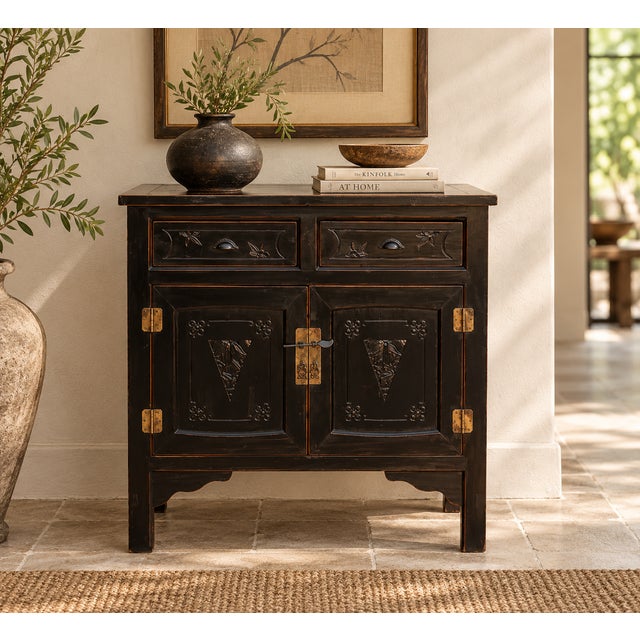 A compact two-door cabinet in black paint, with warm brown showing through at the edges where the finish has worn. Two...