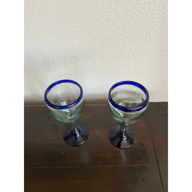 Beautiful pair of artisan hand-blown glass goblets featuring rich cobalt blue rims and matching blue bases. The clear...