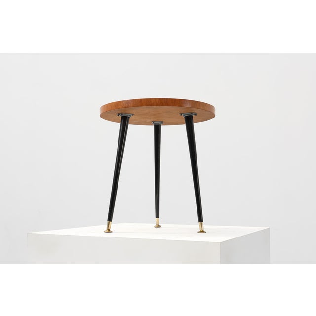 A sleek Italian mid‑century side table from the 1950s, featuring a circular wooden top with a geometric veneer pattern and...