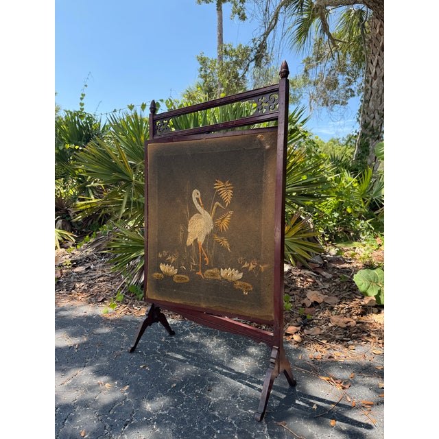 A beautiful antique fireplace screen featuring an intricately embroidered crane and botanical scene, framed in richly...