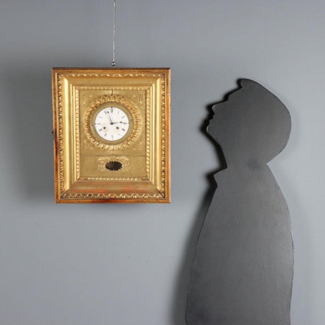 Carved and gilded wooden wall clock with embossed decorations. Enamelled metal dial with Roman numerals, the pendulum...