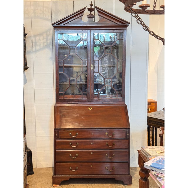 A George III mahogany secretary bookcase with a broken pediment top centered by a carved urn finial. The upper section has...