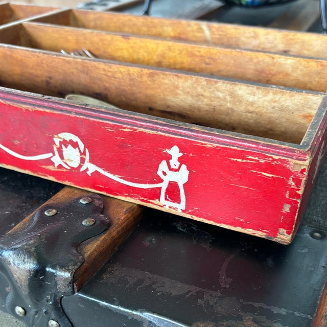 Hand-crafted wooden cutlery tray featuring a vibrant red exterior and stenciled folk art figures. The interior features...