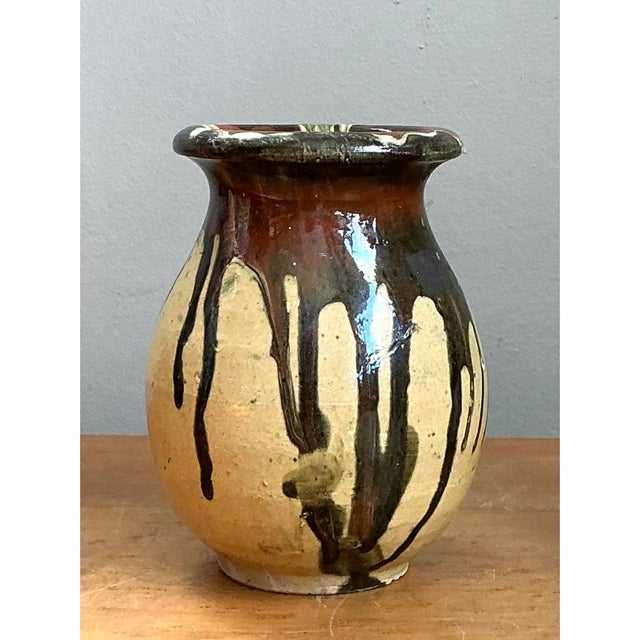 This vintage stoneware vase is a study in organic contrast, where raw clay meets rich, molten glaze. The bulbous, hand-...