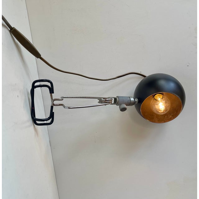 Multi-purpose light fixture with clamp mount. The shade is composed of black lacquered steel with gold-finish to its...
