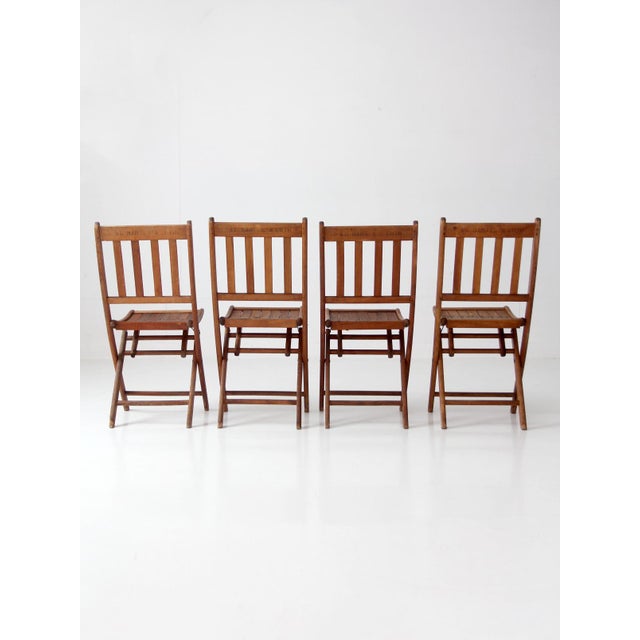 This set of four antique wood folding chairs features slatted wood seats, tall vertical-slat backs, and warm aged...