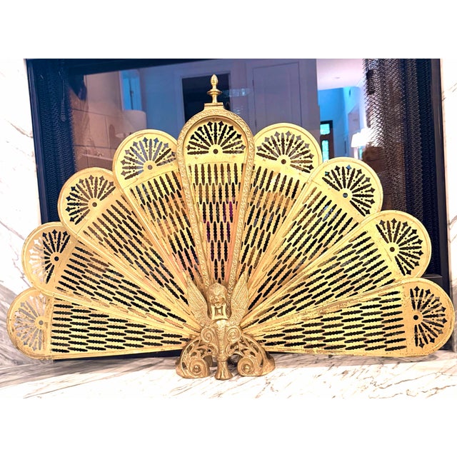 Vintage brass fireplace screen featuring an ornate peacock fan silhouette with intricate pierced detailing and a dramatic...