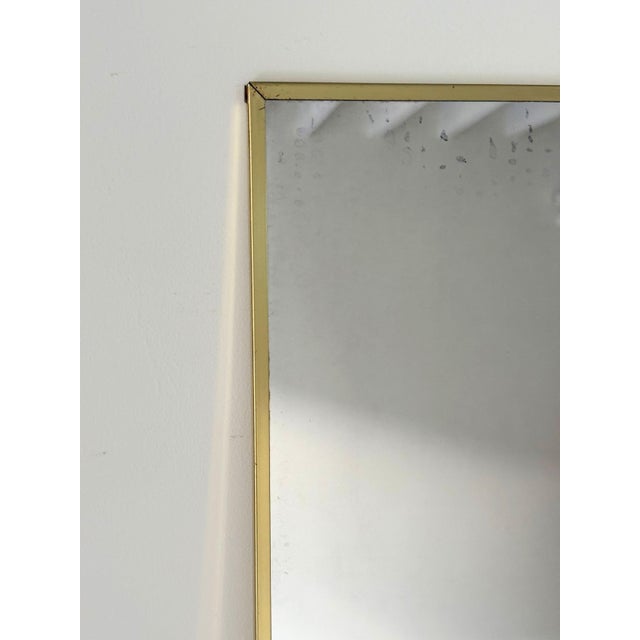 A minimalist vintage wall hanging mirror with a slim hand-wrapped brass frame. The mitred corners are typical of the clean...