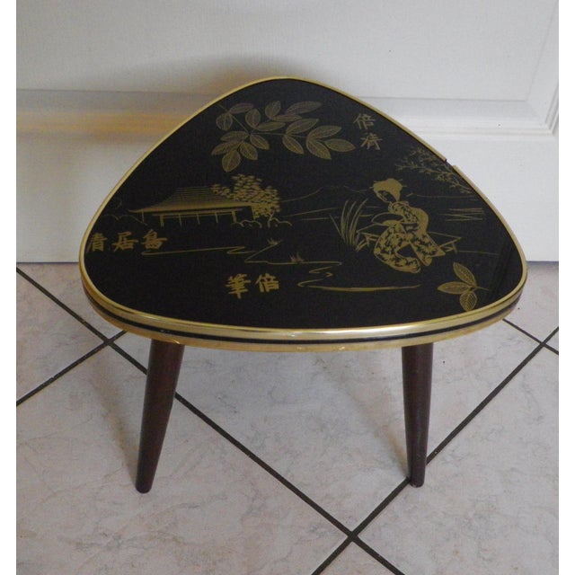 Tripod side table from the 1960s. Wooden compass legs. Guitar pick-shaped top with a gold Japanese-inspired design on a...