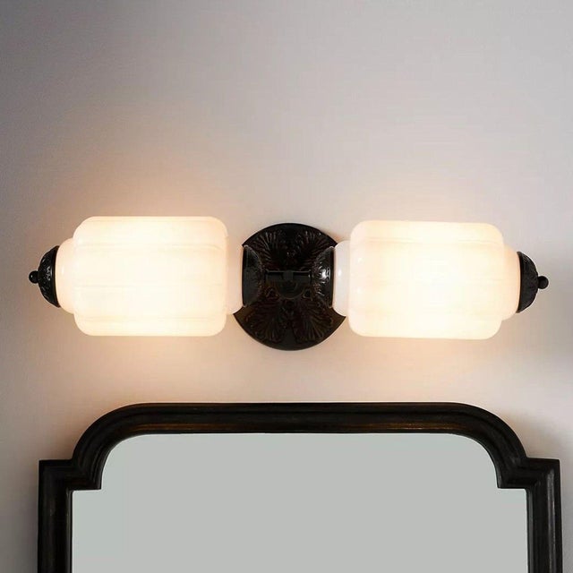 This elegant wall sconce features two white glass shades with a detailed black metal base and end caps. Perfect for...