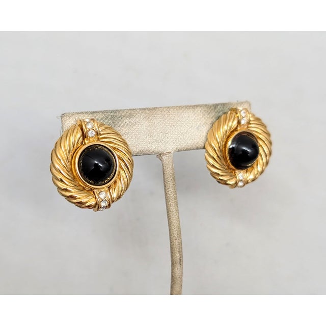 1980s round goldtone cabochon faux-onyx center with "wrapped" design edge with a line of round clear rhinestones at the...