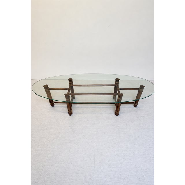 A Vintage McGuire style coffee table with a oval-shaped glass top, bamboo rattan legs and leather-wrapped joints, 1970s...