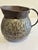 An antique hand hammered copper pitcher with a bulbous riveted body, wide pouring spout, and substantial curved handle....