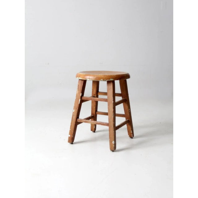 This is a vintage wooden stool. The painted brown wooden low height stool features a round seat with blocky wood legs and...