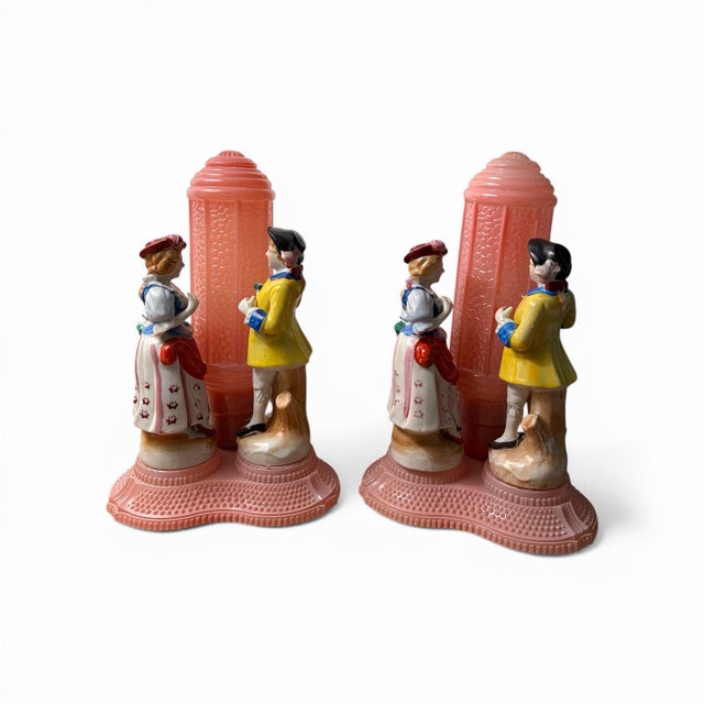 A matched pair of Art Deco table lamps featuring charming figural forms and softly stepped shades in a warm blush tone. A...